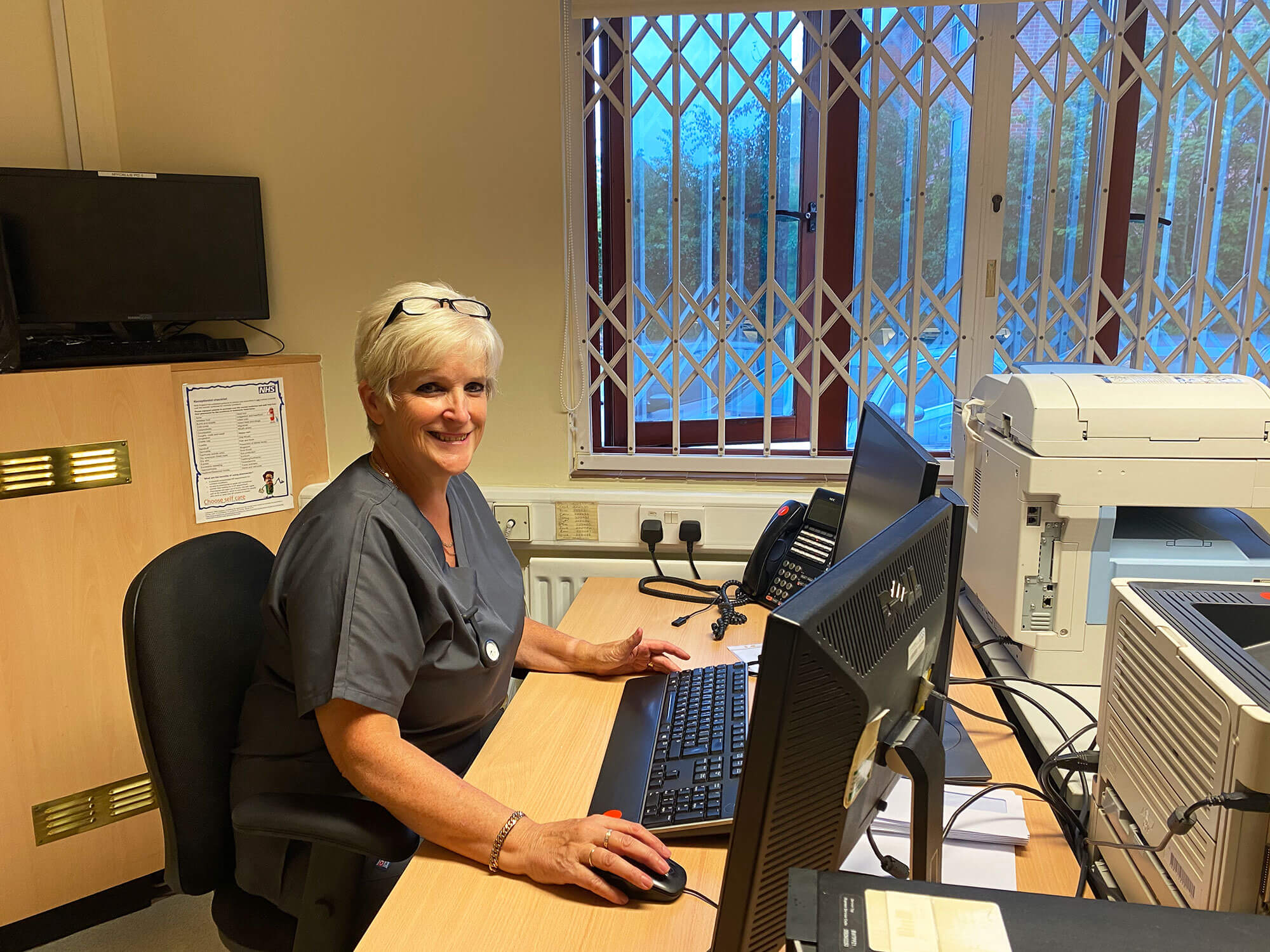 A Moorcroft Medical Centre receptionist sitting at a desk, smiling at the camera