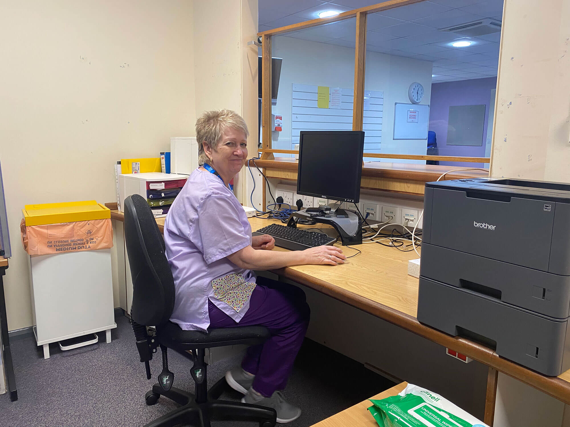 A Moorcroft Medical Centre team member sat at a desk smiling at the camera